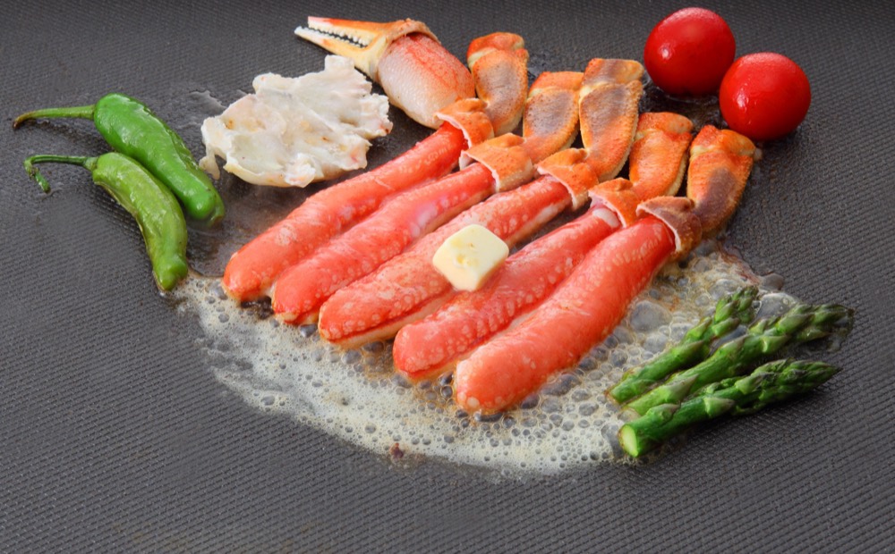 鉄板の上でバターとともに焼かれている、生ずわいがにの脚肉
